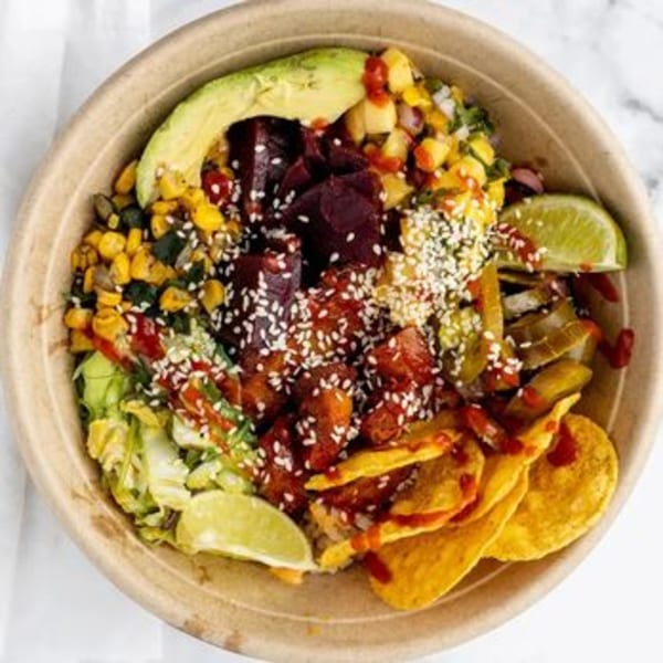 Colorful poke bowl with avocado, corn, beets, tuna, sesame seeds, lime, and tortilla chips.