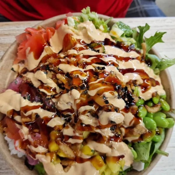 Close-up of a Poke Mahi poke bowl, generously drizzled with two sauces, showcasing fresh ingredients.