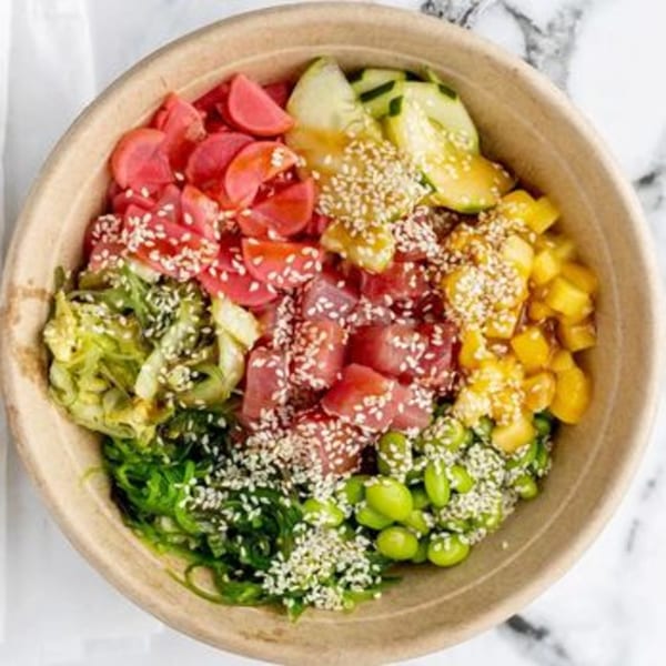 A colorful poke bowl with tuna, mango, cucumber, seaweed, edamame, and pickled radishes, topped with sesame seeds.