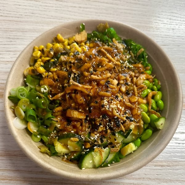 A Poke Mahi poke bowl filled with corn, edamame, cucumbers, scallions, and a savory sauce.