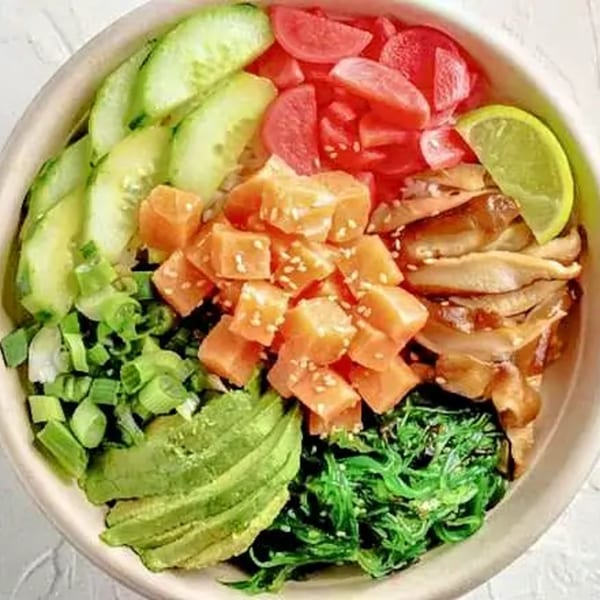 A vibrant Poke Mahi bowl with salmon, cucumber, avocado, seaweed, pickled radish, and chicken.